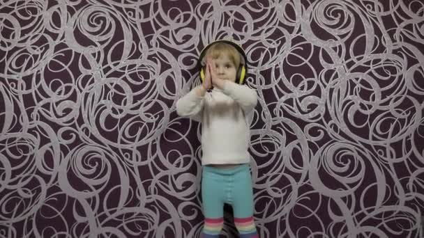 Маленький счастливый ребенок прыгает и танцует на диване и слушает музыку в наушниках — стоковое видео