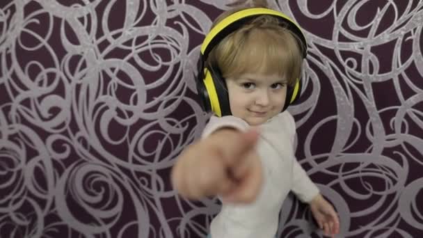 Pequena criança feliz dançando no sofá e ouvindo música em fones de ouvido em casa — Vídeo de Stock