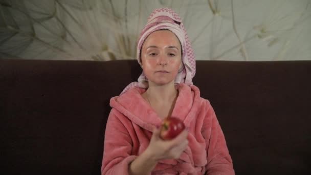 Mujer viendo una película nocturna en la televisión, comiendo una manzana. Albornoz, máscara facial — Vídeos de Stock