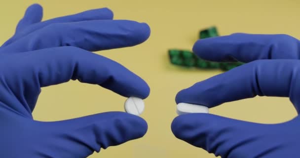 One oval and one round white pills in hands dressed in blue medical glove — Stock Video