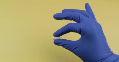 Elinde kauçuk steril tıbbi eldiven giymiş bir oval beyaz hap