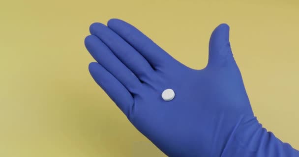 Eine runde weiße Pille in der Hand in einem sterilen medizinischen Gummihandschuh — Stockvideo