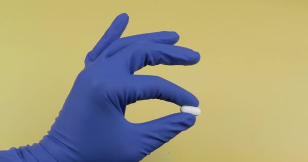 Ένα οβάλ λευκό χάπι στο χέρι ντυμένος σε ελαστικό αποστειρωμένο ιατρικό γάντι — Αρχείο Βίντεο
