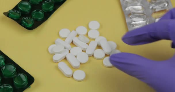Велика кількість білих круглих і овальних таблеток. Рукавички для стерильних рукавичок піднімають таблетки — стокове відео
