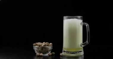 Bira siyah arka plan üzerinde cam içine dökülüyor. Antep fıstığı kase