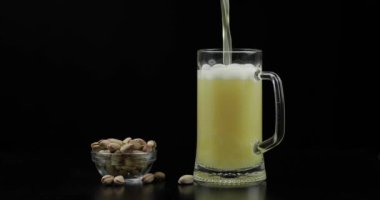 Bira siyah arka plan üzerinde cam içine dökülüyor. Antep fıstığı kase