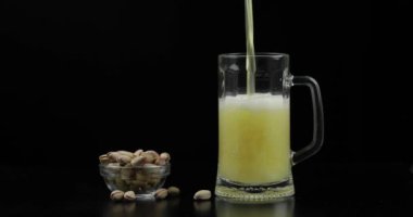 Bira siyah arka plan üzerinde cam içine dökülüyor. Antep fıstığı kase