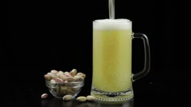 Bira siyah arka plan üzerinde cam içine dökülüyor. Antep fıstığı kase