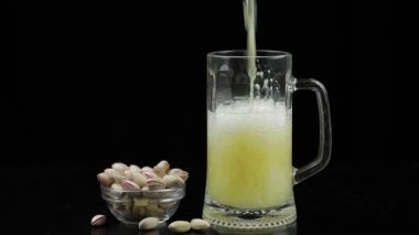 Bira siyah arka plan üzerinde cam içine dökülüyor. Antep fıstığı kase