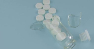 Mavi arka planda dönen birçok hap ve ilaç ile Kırık cam kavanoz