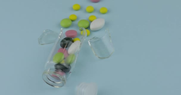 Frasco de vidro quebrado com muitas pílulas diferentes e drogas girando em fundo azul — Vídeo de Stock