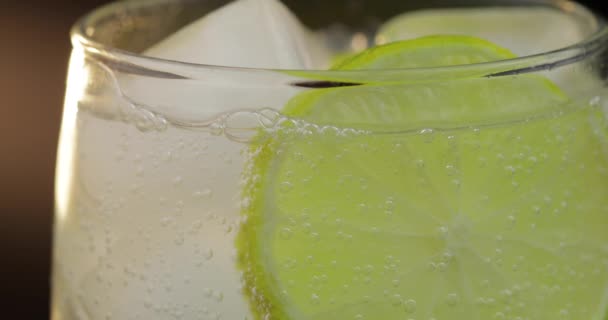 Close-up of a refreshing drink soda with bubbles interacting with ice and lime — Stock Video