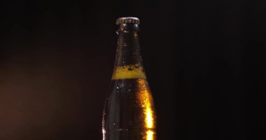 Siyah bir arka plan üzerinde soğuk bira şişesi. Yavaşça dönüyor. Kondens