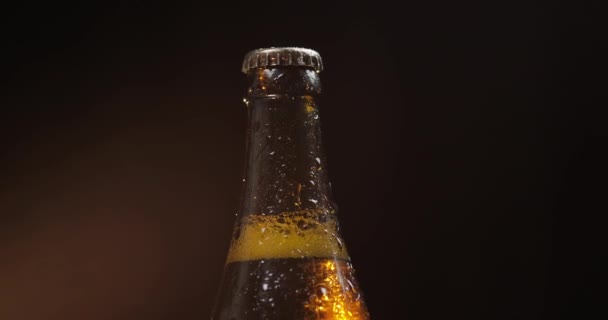 Botella de cerveza fría sobre fondo negro. Rota lentamente. Condensado — Vídeo de stock