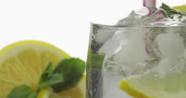 Stiring in a glass with cold drink, leaves of mint, lime, lemon and ice cubes — Stock Video