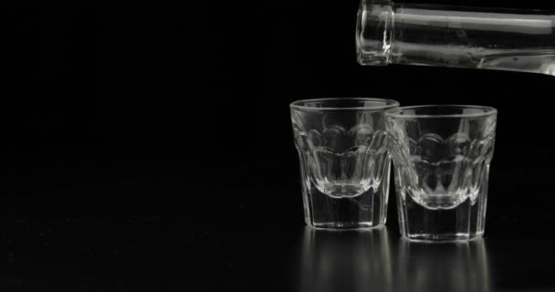 Zwei Schuss Wodka aus einer Flasche in Glas gießen. schwarzer Hintergrund — Stockvideo