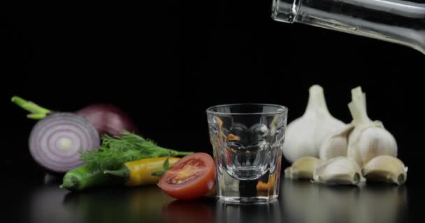 Giet alcohol drinken wodka uit een fles in shot Glass. Achtergrond met groenten — Stockvideo