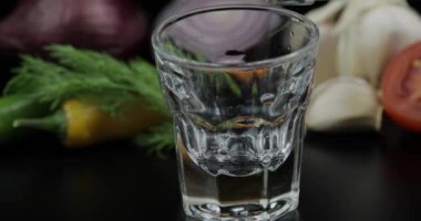 Bardak bir şişeden alkol içecek votka dökün. Sebzeli arka plan