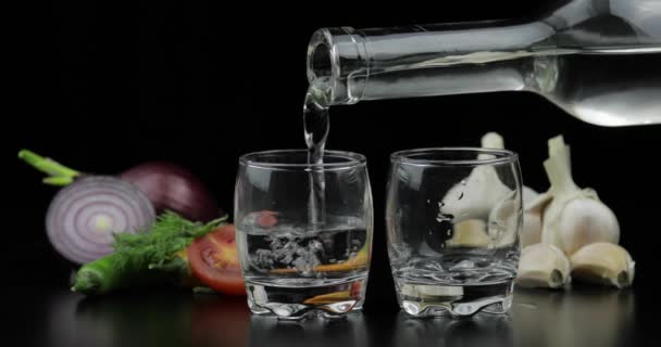 Vierta el vodka de alcohol de una botella en dos vasos de chupito. Fondo con verduras — Vídeos de Stock