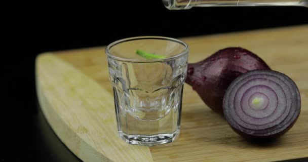 Wodka aus einer Flasche in Schnapsglas auf Schneidebrett mit Zwiebeln gießen — Stockvideo