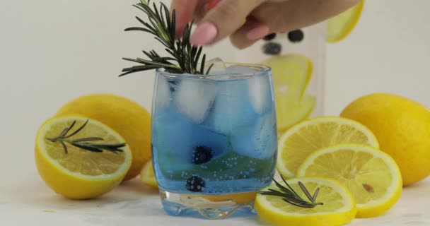 Lägga citronskiva, rosmarin, halm i ett glas med soda lemonad blå cocktail — Stockvideo