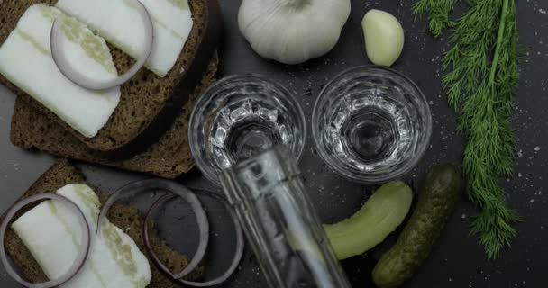 Pour alcohol drink vodka from a bottle in two shot glass. Surface with snacks — Stock Video