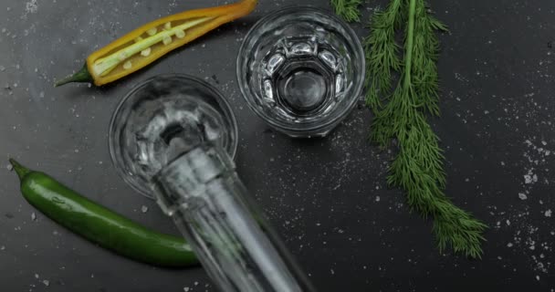 Pour alcohol drink vodka from a bottle into two shot glass. Surface with snacks — Stock Video