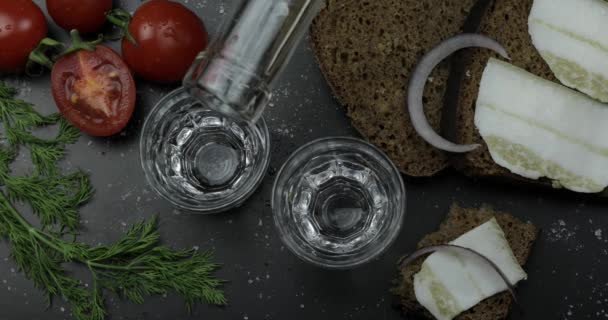 Vodka bebida de álcool de aguaceiro de uma garrafa em dois copos de tiro. Superfície com lanches — Vídeo de Stock