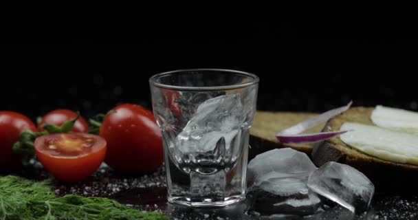 Wodka aus einer Flasche in Schnapsglas gießen. Oberfläche mit Snacks — Stockvideo