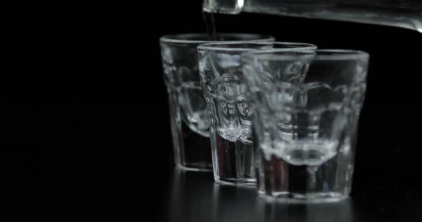 Hälla upp tre skott av vodka från en flaska i glas. Svart bakgrund — Stockvideo