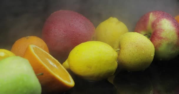 Тропический лимон, апельсин, яблоко в облаках холодного льда тумана дыма на темном фоне — стоковое видео