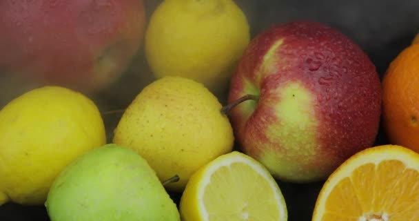 Tropische citroen, sinaasappel, appel in koud ijs wolken van mist rook op donkere achtergrond — Stockvideo