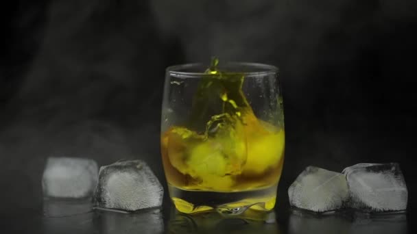 Whiskey jéggel. Jégkockák hozzáadása fekete háttérrel. Egy pohár rum-alkohol — Stock videók