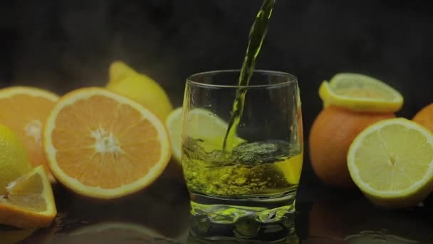 Vierta el jugo en rodajas de vidrio, naranja y limón sobre el fondo. Movimiento lento — Vídeo de stock