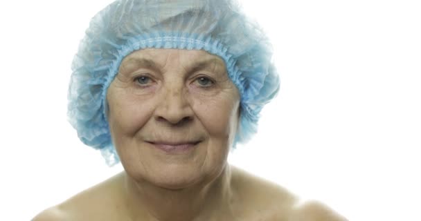 Пожилая женщина в защитной шляпе. Врач делает уколы лица пациенту — стоковое видео