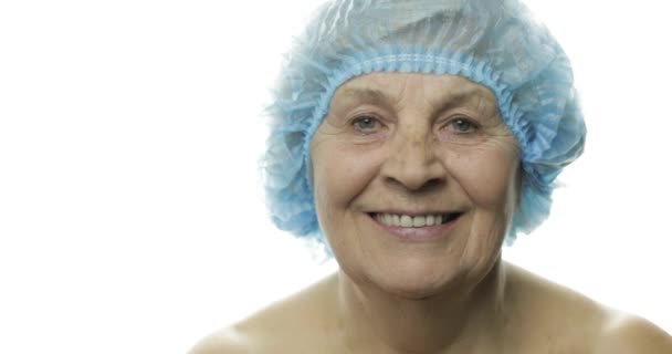 Пожилая женщина в защитной шляпе. Врач делает уколы лица пациенту — стоковое видео