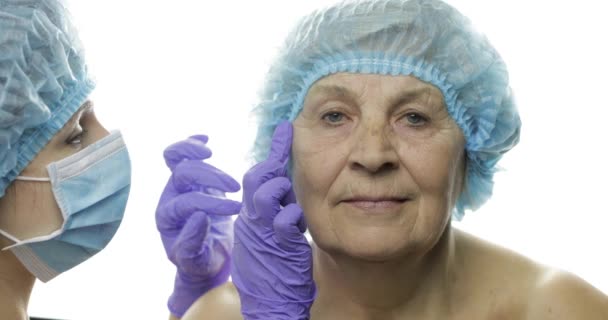 Smiling elderly female in protective hat. Plastic surgeon checking woman face — Stock Video