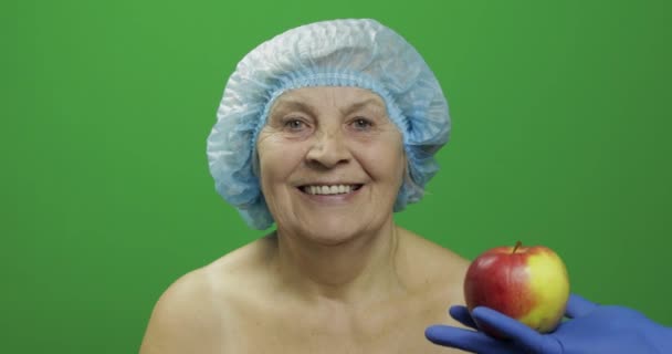 Mujer anciana con sombrero protector. El doctor le muestra una manzana. — Vídeo de stock