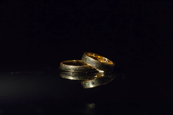 Anillos de boda que yacen en la superficie oscura brillando con luz. Salpicaduras de agua —  Fotos de Stock