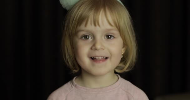 Primer plano de una pequeña rubia linda cara de chica. Chica sonriendo. Adentro. Retrato plano — Vídeo de stock