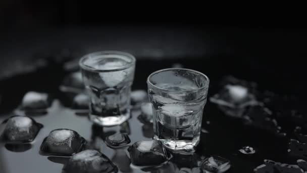 Añadir cubitos de hielo a la toma de vodka en vidrio sobre fondo negro. Bebida alcohólica — Vídeos de Stock