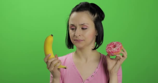 Empezando una alimentación saludable. Dile que no a la comida chatarra. Elección de rosquilla o plátano para comer — Vídeos de Stock