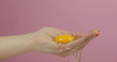 Kadın elinde taze yumurta. Manikür el pembe arka plan üzerinde yumurta sarısı tutar