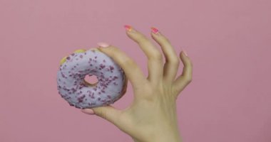 Kadınların elleri mavi, lezzetli, pembe arka planda serpiştirilmiş donut tutuyor..