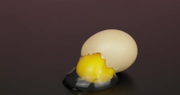 Яйцо желток выливается из сломанной яичной скорлупы на черную поверхность — стоковое видео