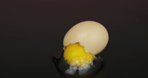 Egg yolk poured out from broken eggshell on black surface — Stock Video