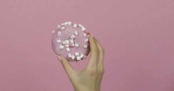 Женские руки держат розовый, вкусный, посыпанный пончик на розовом фоне . — стоковое видео