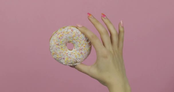 Mão das mulheres segurando branco, delicioso, donut polvilhado no fundo rosa . — Vídeo de Stock