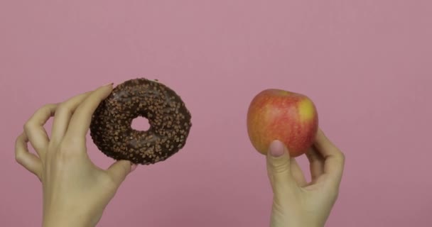 Τα χέρια κρατούν ντόνατ και μήλο. Επιλογή ντόνατ εναντίον μήλου. Υγιεινό ή πρόχειρο φαγητό — Αρχείο Βίντεο