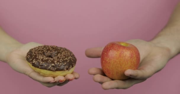 Ruce drží koblihu a jablko. Výběr koblihu proti jablku. Zdravé nebo podřadné potraviny — Stock video